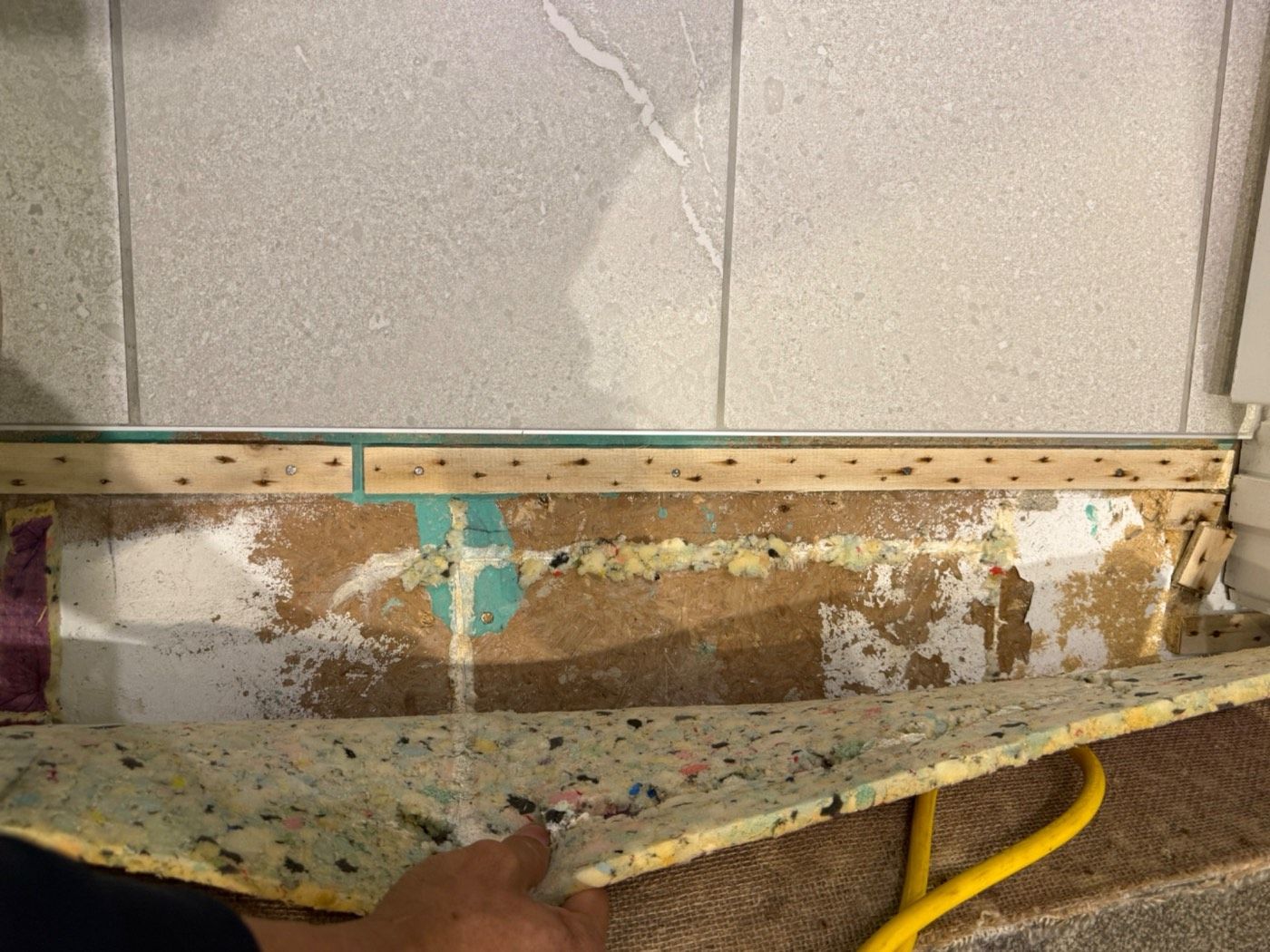 Flooring lifted at the bathroom doorway, showing wet underlay and framing beyond