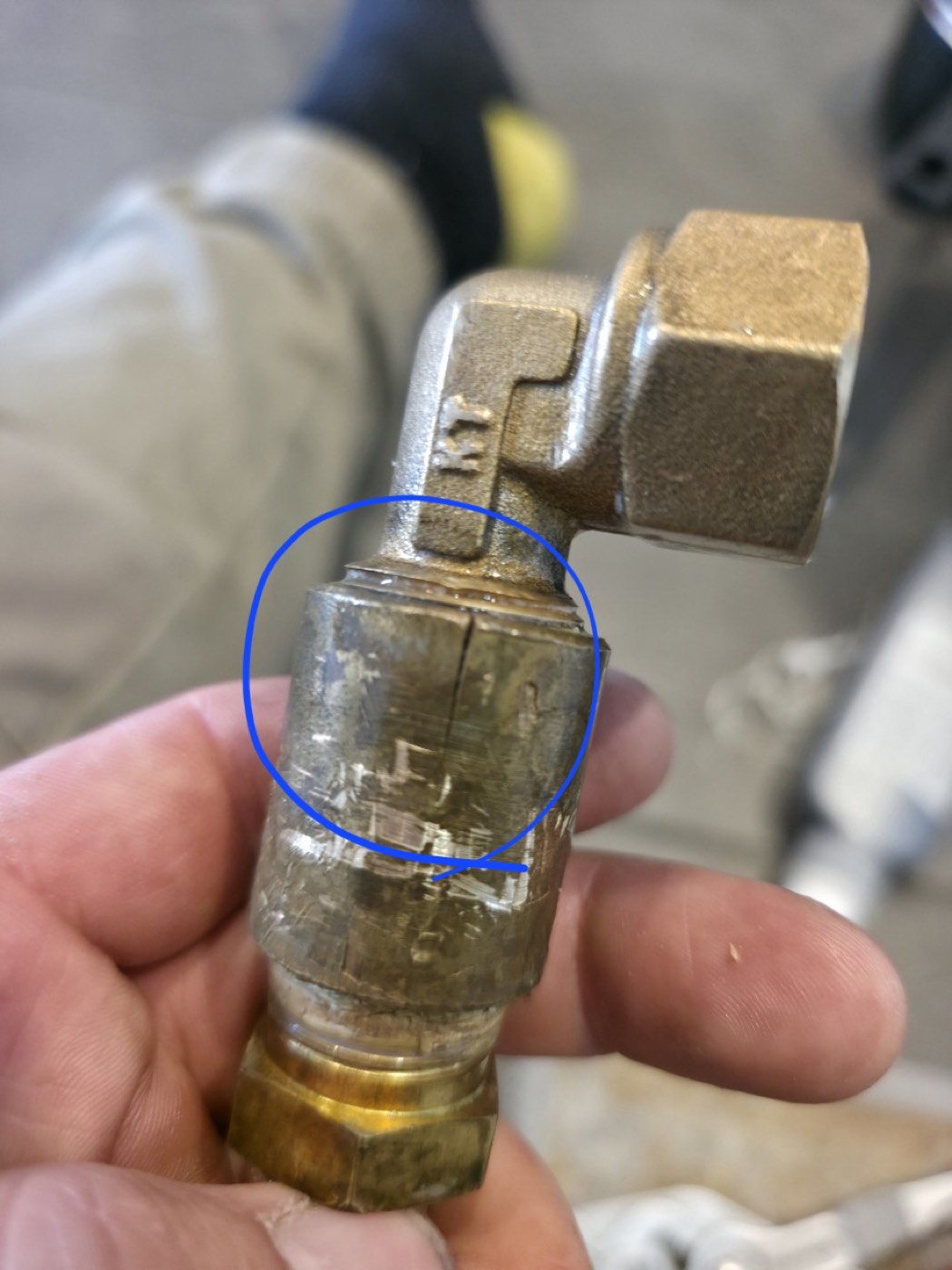 A cracked 15mm brass gas fitting removed from under a cooktop, with the crack circled