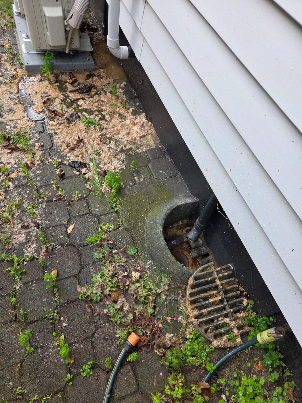 Overflowing gully trap beside a house with the grate lifted and waste spread across the paving