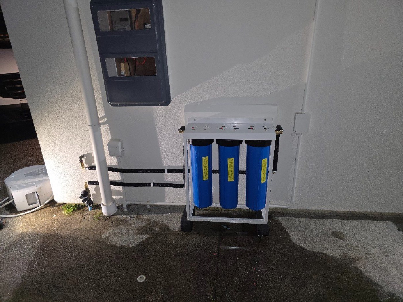 A three-stage jumbo whole-house water filter on a freestanding frame outside a house in Henderson, connected to the main