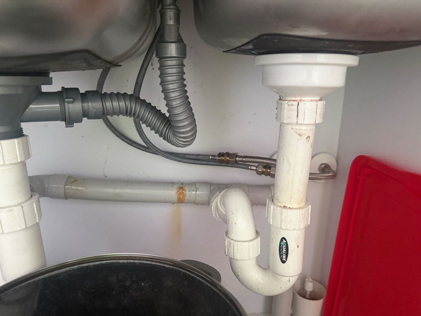 Under a kitchen sink showing the waste pipes, trap and the flexible supply tail feeding the mixer
