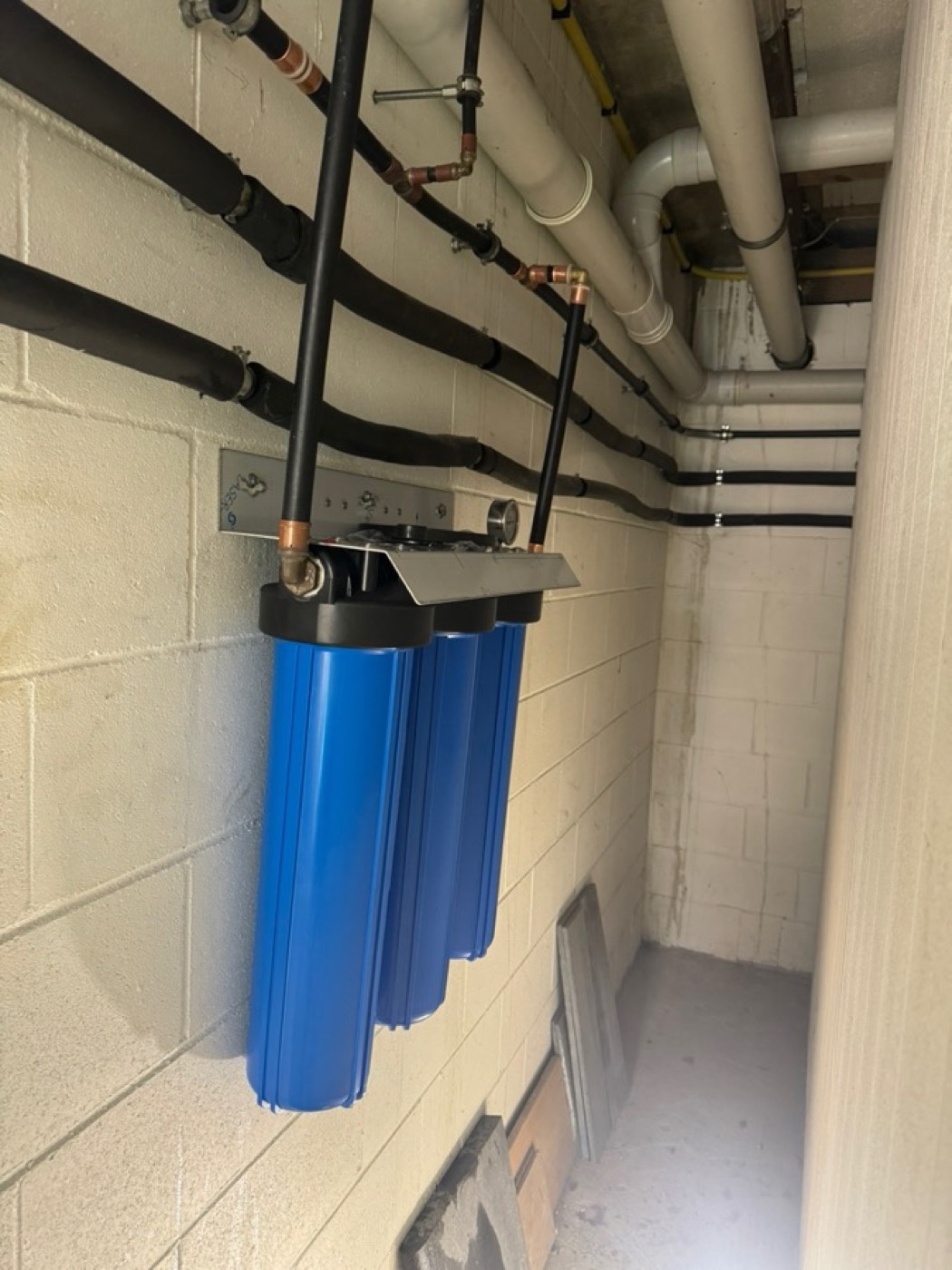 A three-stage 20 inch Big Blue whole-house water filter mounted on a plant room wall