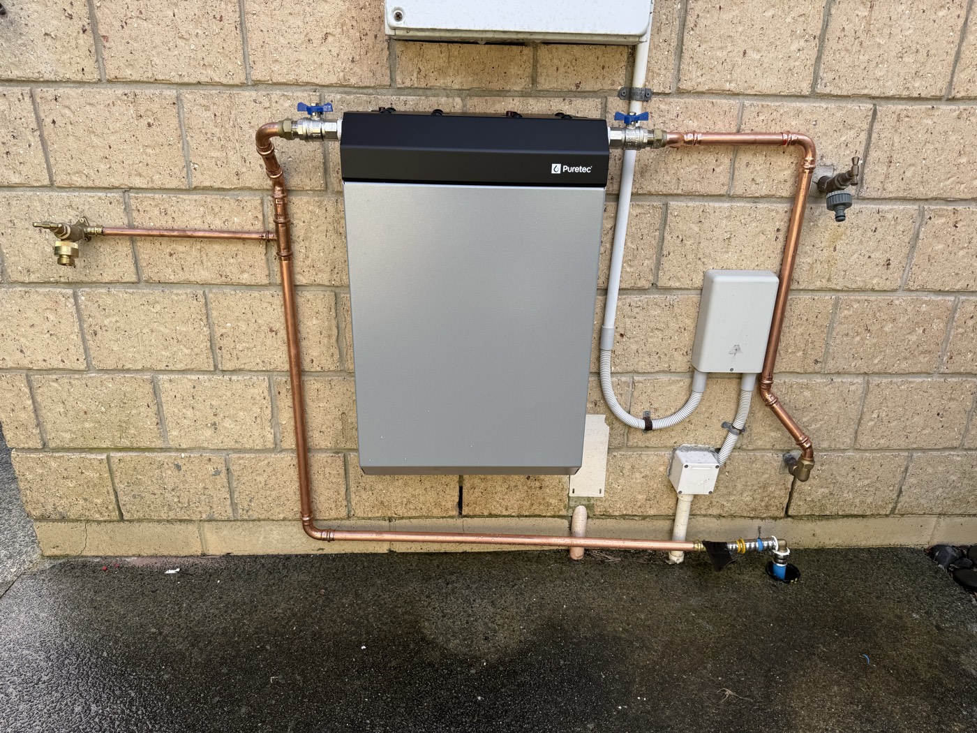 The finished Flat Bush whole-house filter with its cover on, copper pipework clipped to the brick wall and the garden tap on the supply side
